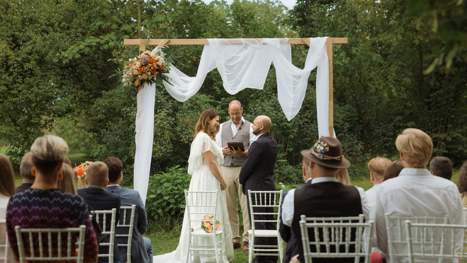 Paar heiratet unter einem Holzbogen mit Publikum im Garten