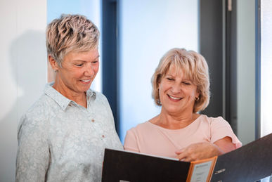 Zwei Mitarbeitende besprechen sich auf dem Flur der Kanzlei, Fenster im Hintergrund.