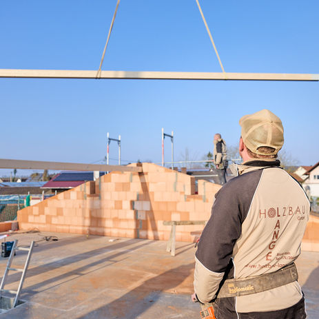 Ein Bauarbeiter beobachtet wie ein Kran einen Holzbalken bewegt