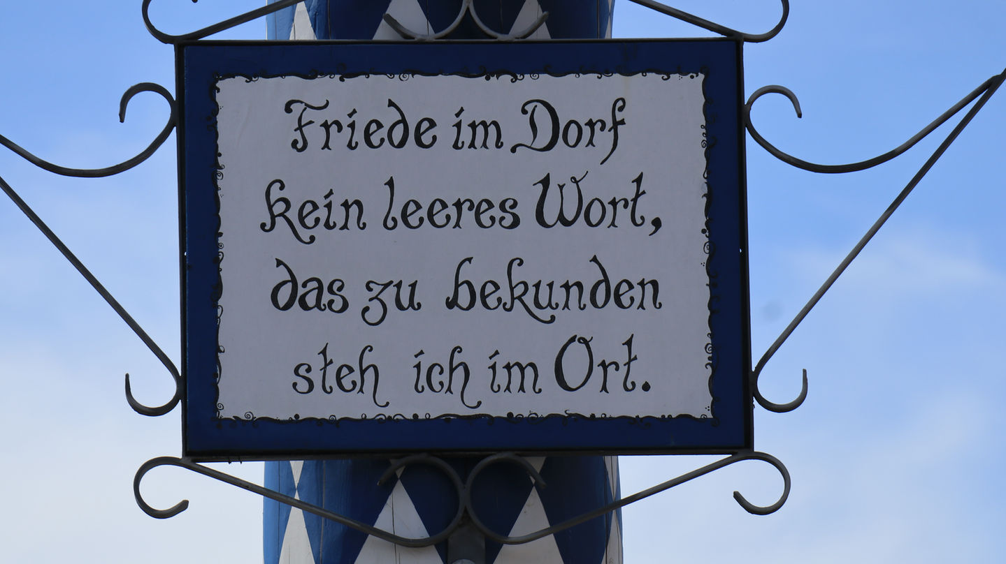 Schild mit Text: Friede im Dorf, kein leeres Wort, das zu bekunden steh ich im Ort.