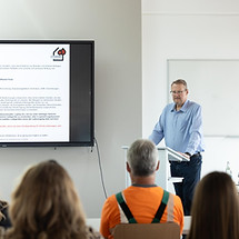 Schulungssituation- Werner Scheck steht an einem Pult und spricht mit Mitarbeitenden einer Firma über das Thema Brandschutz