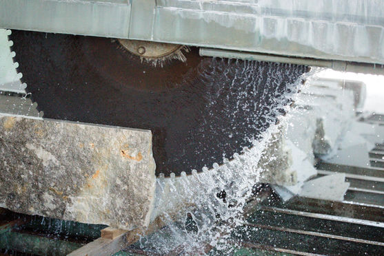 Kreissäge schneidet Stein, Wasser spritzt, im Hintergrund weitere Steine. Böswald Natursteinwerk.
