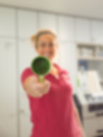 Lachende Frau in rotem Shirt hält grüne Tasse in die Kamera.