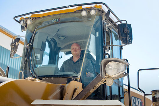Man in CAT excavator smiles at the camera while working.