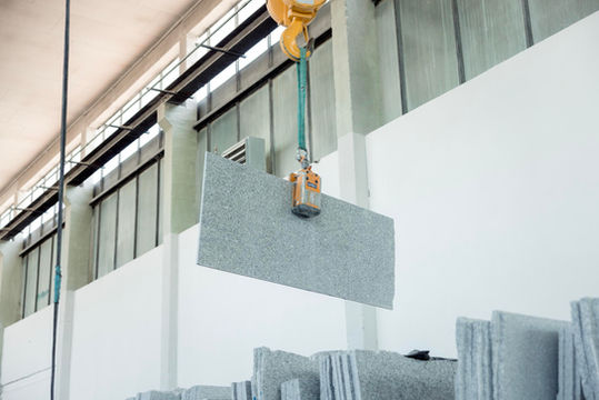 A crane lifts a grey stone slab in the factory.