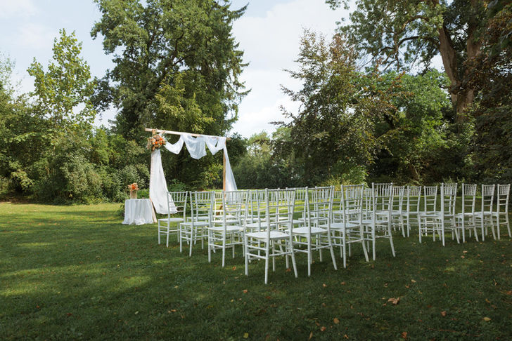 Der Garten wurde für eine frei Trauung hergerichtet. Weiße Stühle stehen für die Gäste vor einem Geschmückten Holzbogen. Seitlich ist ein kleiner Tisch mit Blumen und der Ringschatulle