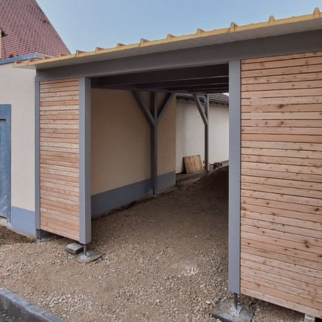 grauer Carport mit Blockhauswand beim Eingang