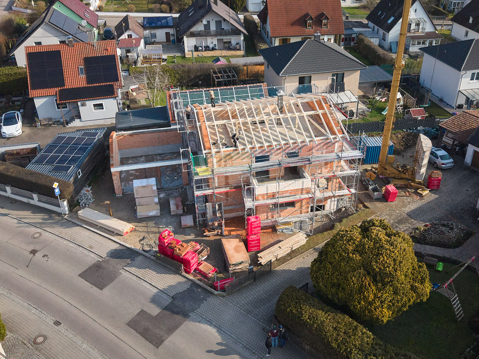 Drohnenaufnahme von einer Holzhaus Baustelle. Drumherum stehen Wohnhäuser.