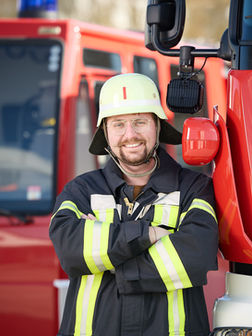 1. Kommandant Stefan Meckermann lehnt an einem Feuerwehrauto und lächelt in die Kamera.