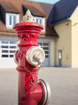 Ein roter Hydrant vor dem Gebäude der Feuerwehr.