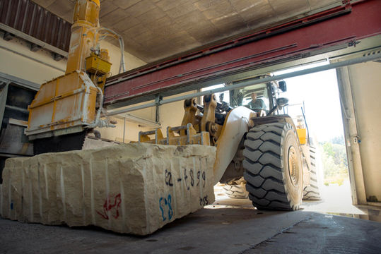 Yellow excavator cutting a large block of stone, with numbers, Böswald natural stone works.