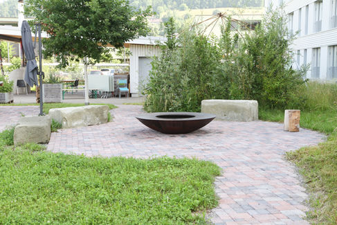 Sitzplatz mit Sandsteinblöcken rund um eine Feuerschale und organisch verlegten Verbundsteinen. Stiftung Aarhus, Gümligen.