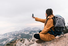 smiling-young-female-hiker-sitting-top-mountain-taking-selfie-mobile-phone.jpg