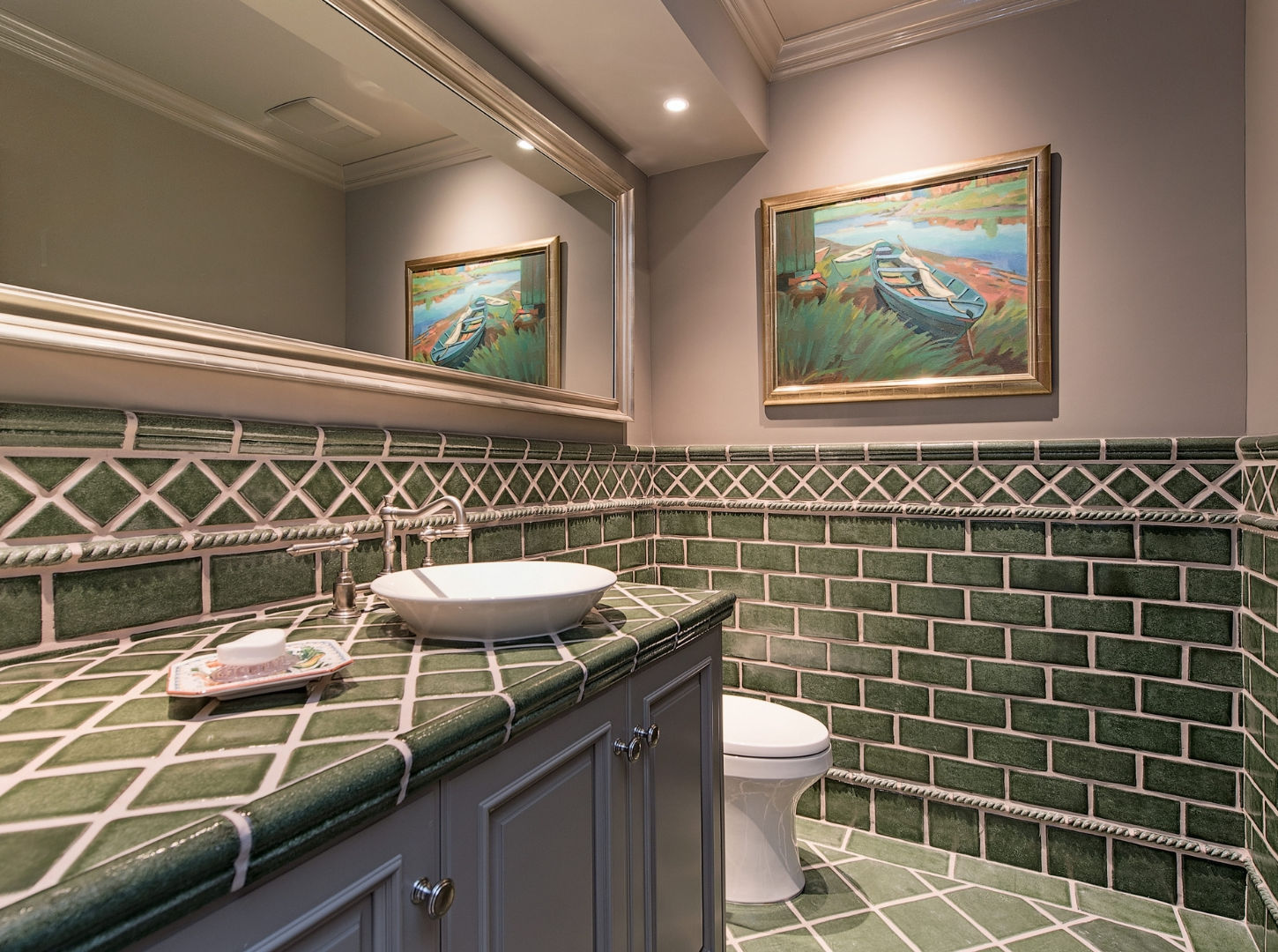 Secondary bathroom with green tile wainscoting, vessel sink, mirror, and framed artwork.