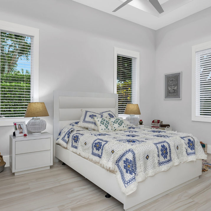 Secondary bedroom with crisp white furnishings, oversized corner windows, and soft blue textiles that bring a fresh coastal palette to the airy retreat.