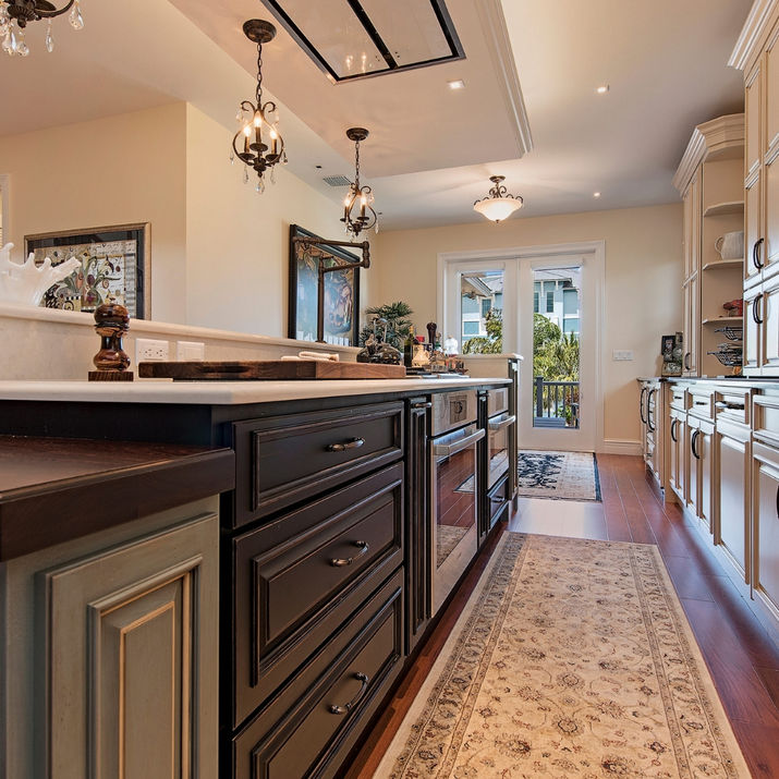 Dark wood island with cream cabinetry, stone backsplash, and pendant lighting in luxury kitchen.