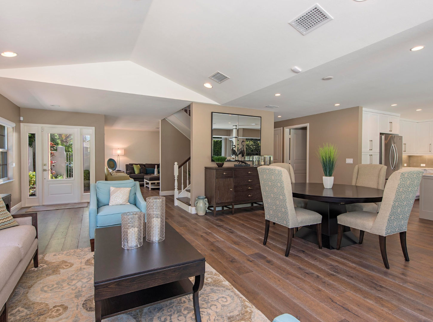 Open great room with living, dining, and kitchen areas, wood flooring, and entryway views.