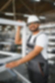 Happy bearded Indian male factory worker in special uniform and white hard hat holding a.j