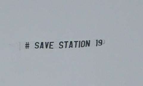 Sky banner featuring the message "# SAVE STATION 19" in black block letters, flying against a pale overcast sky, created in collaboration with The Skywriters, showcasing precision aerial advertising and high-impact event marketing.