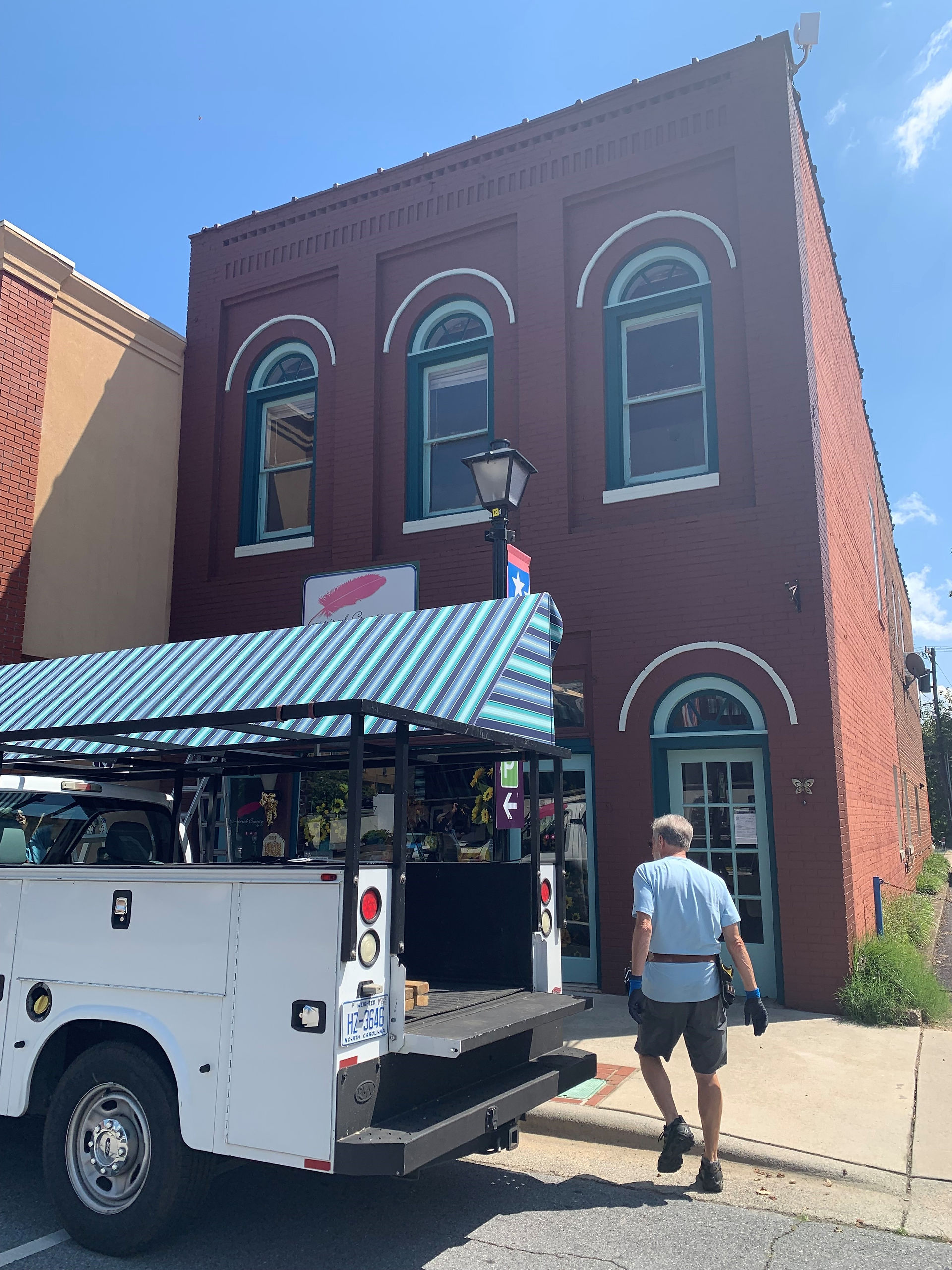 Maroon brick building, teal trim windows, truck with striped awning, person entering.