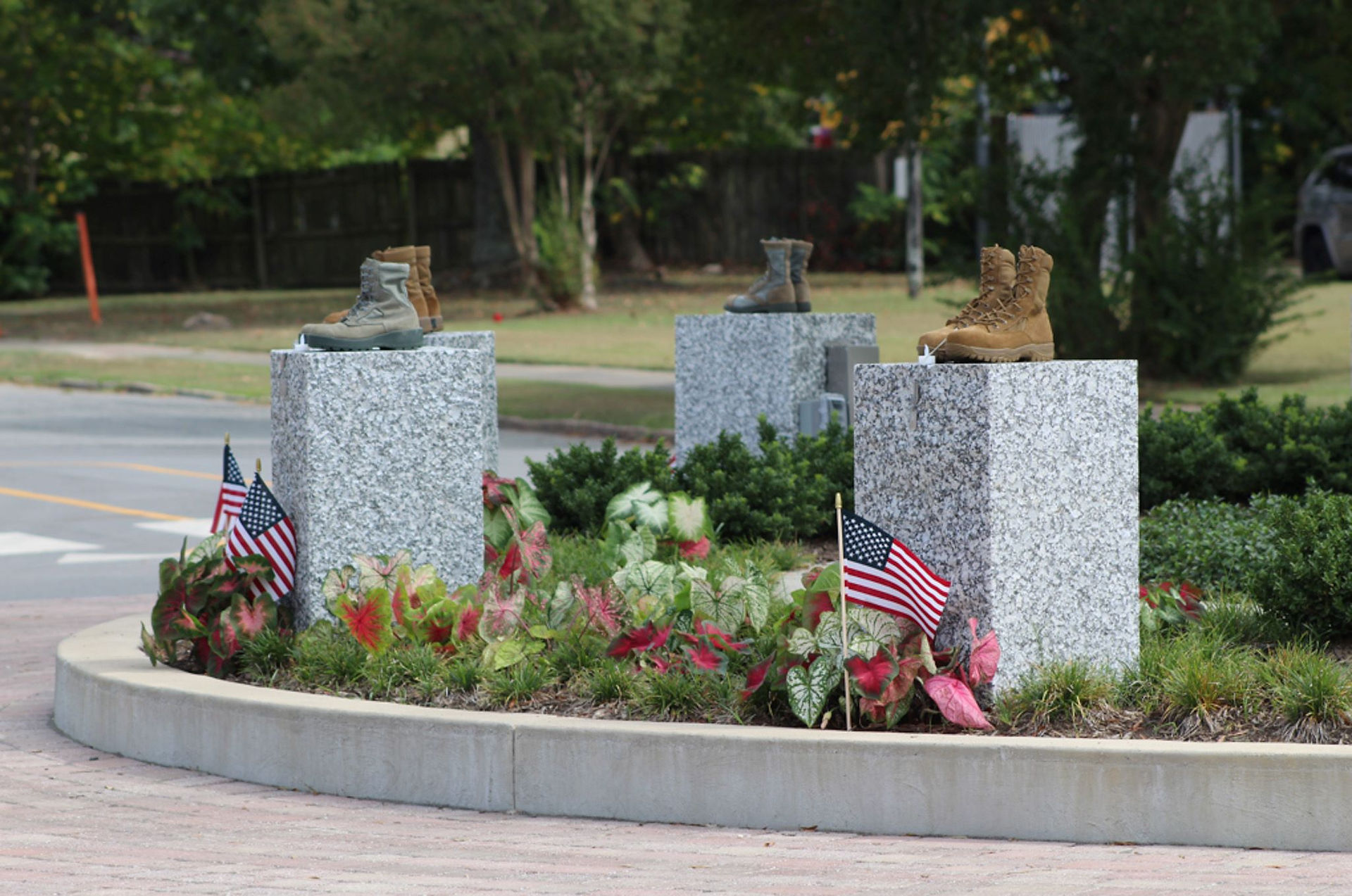 Three pairs of military boots on stone pedestals with American flags.