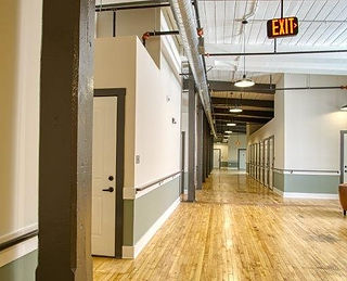 Long, empty industrial hallway with wooden floor and red EXIT sign.