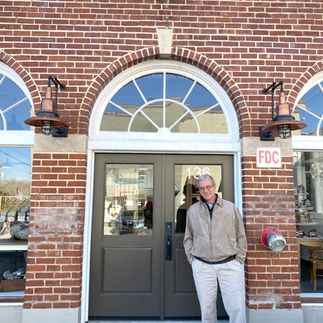 Man stands smiling before arched brick building with FDC sign.