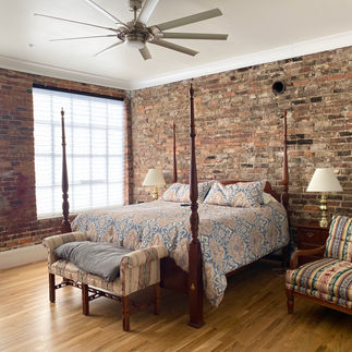 Cozy bedroom with wooden four-poster bed, exposed brick wall, ceiling fan.