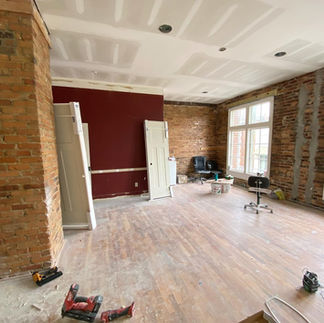 Renovating empty room with exposed brick walls, red accent, and hardwood floor.