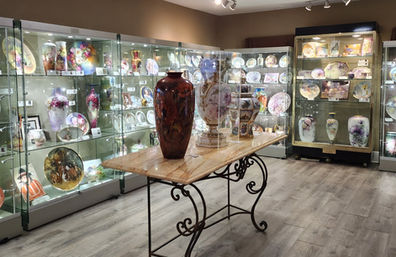 The interior of a museum with multiple display cases lit up.  In the for ground there is a table with large vases.