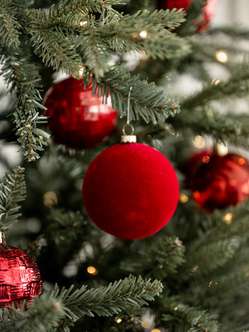 Red ornaments hanging among softly lit Christmas tree branches.