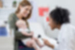 A mother holds a baby while a doctor checks the baby's reflexes.