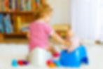 A child sitting on a potty chair next to a doll on a potty chair
