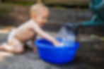 A baby reaches for water being poured from a watering can