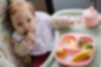 A baby sits with a plate of finger foods