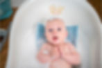 A calm baby lies in a baby tub with soapy water.