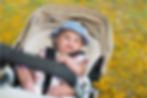 A cheerful baby rides in a stroller outside.