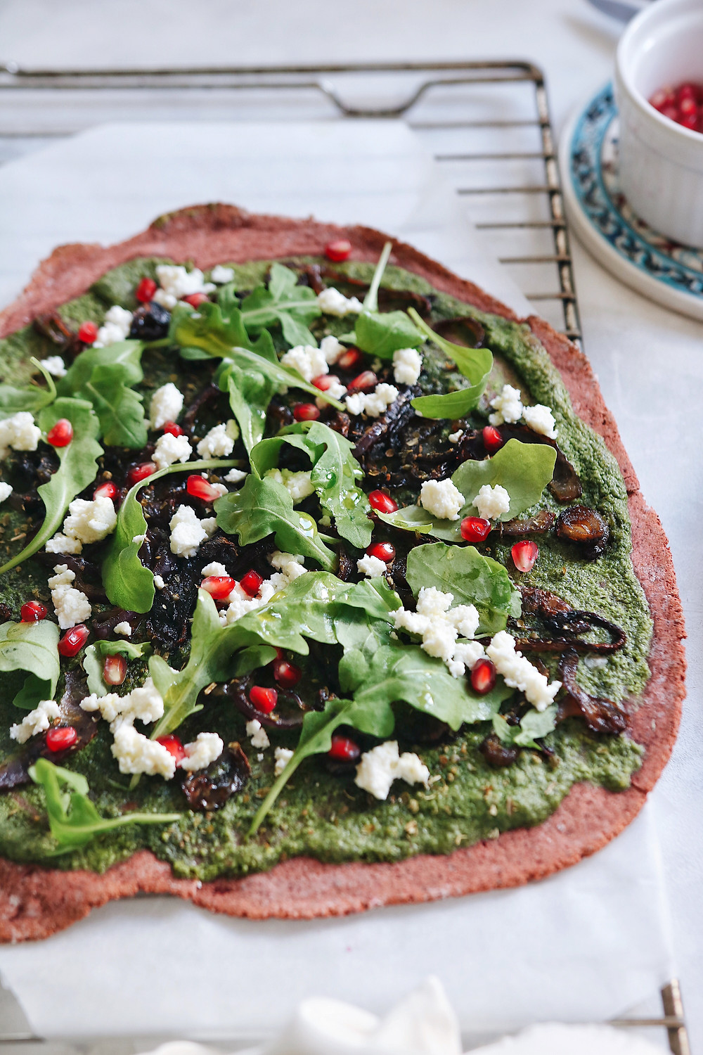 A closeup of the toppings on the beetroot crust pizza, arugula pesto, fresh arugula, ricotta cheese and pomegranate seeds.