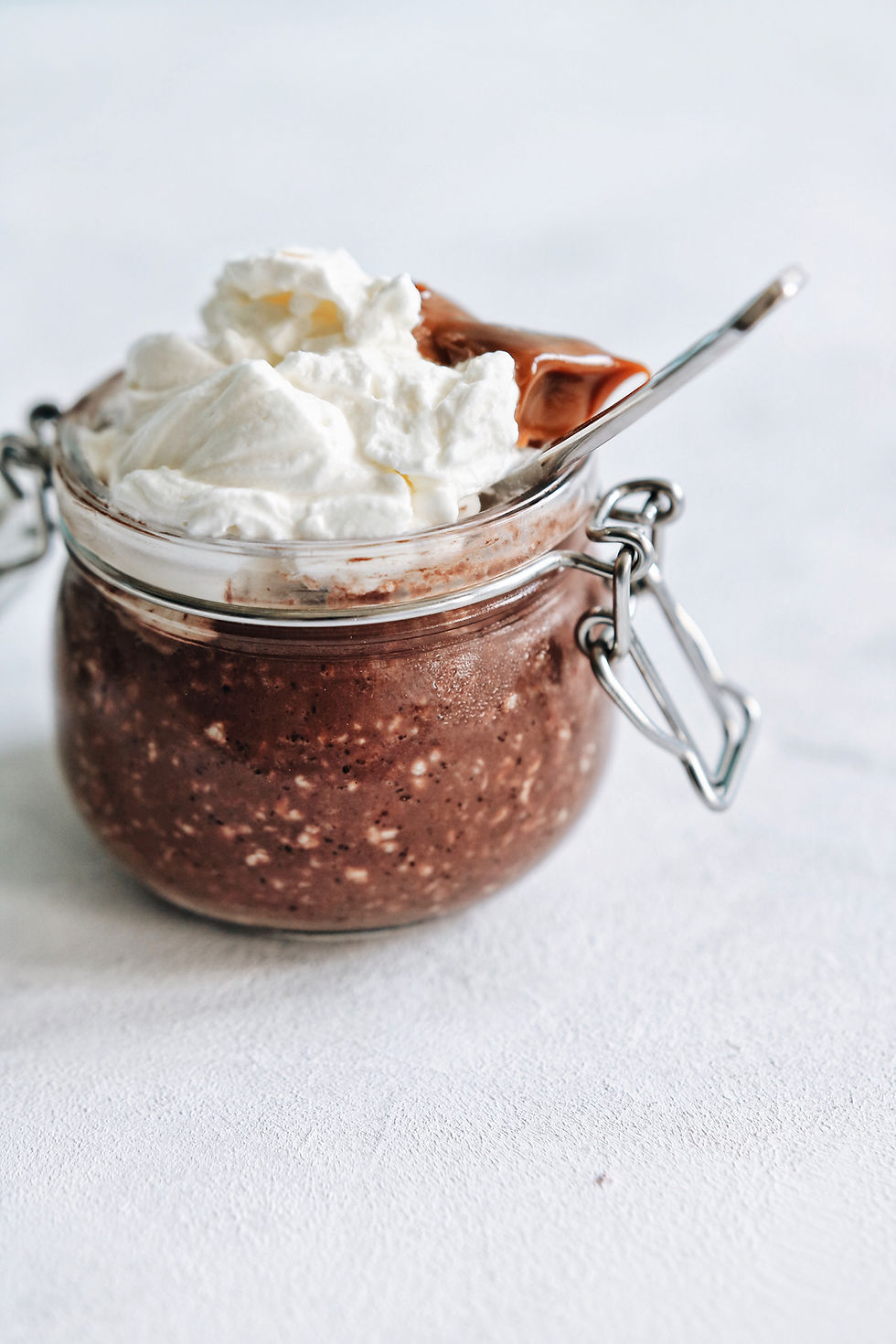 A gluten free chocolate oatmeal in a glass jar, with whipped cream and dulce de leche on top.