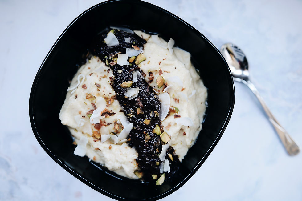 Grain free coconut porridge in a black bowl, topped with melted chocolate coconut and pistachios, a spoon in the background.
