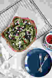 A beetroot crust pizza on a white backround, a cooling rack, blue plate and pomegranate seeds on the side.