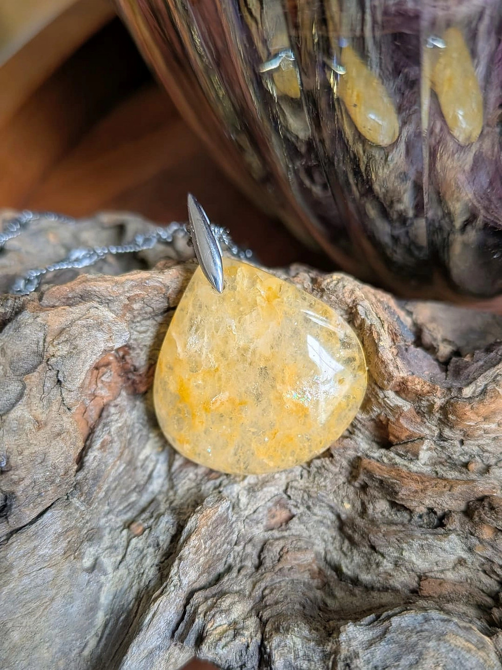 Pendentif en aventurine jaune orangée, percée à l'atelier, avec bélière argent, déposé sur un bois naturel brut.