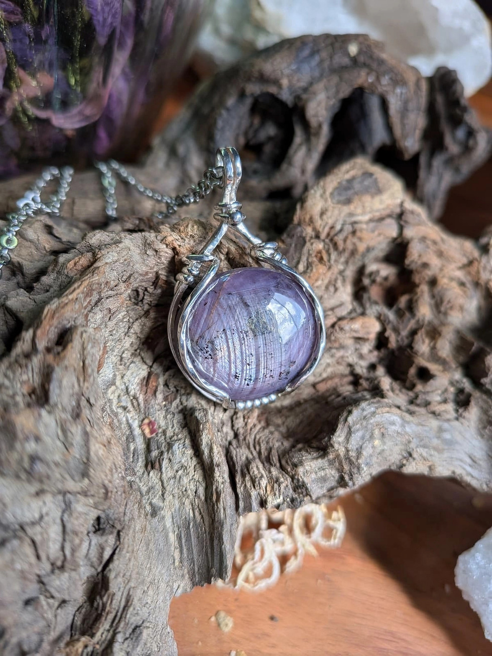 Saphir mauve étoilé, wrapping artisanal en argent,  déposé sur un support en bois naturel brut.