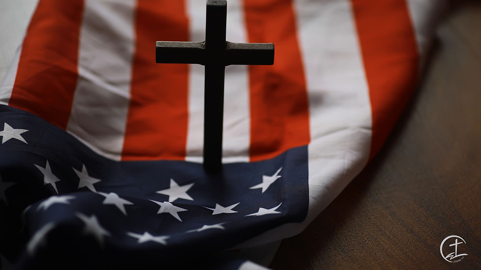 American flag laying on a table with a small cross standing on the flag.