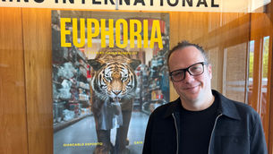A man in glasses stands smiling by a movie poster for "Euphoria" featuring a tiger. Sign above reads "KINO INTERNATIONAL."