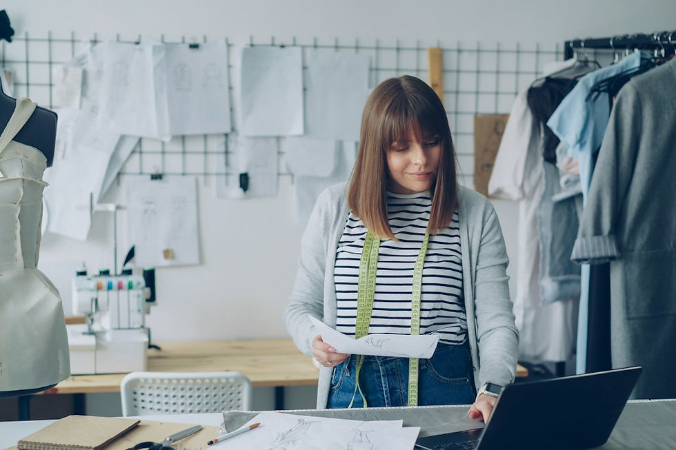 Fashion designer reviewing sketches and a laptop while planning a collection