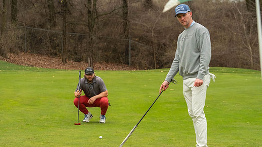 Two Golfers on the puttign green reading a putt