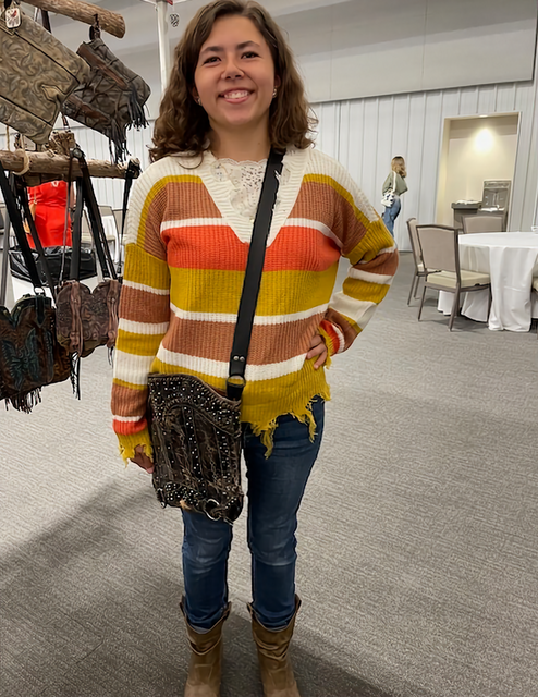 Woman wearing striped sweater poses with a purse at a convention smiling