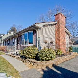 A side view of this tan one level ranch in Chicopee has a large front yard. The shutters are brown, as is the front door, and there is a bow window on the right side. The driveway to the right of the house, has a walkway off of it to the front door.