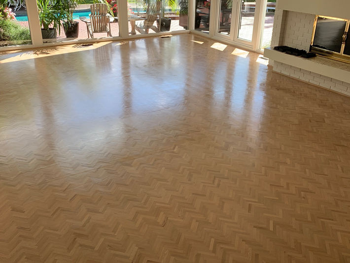 Luxury refinished herringbone parquet hardwood floors in sunroom conservatory – high-gloss oak chevron pattern with stunning pool and garden views through glass walls.